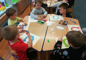 Dzieci przy stolikach kolorują kredkami podkowy.